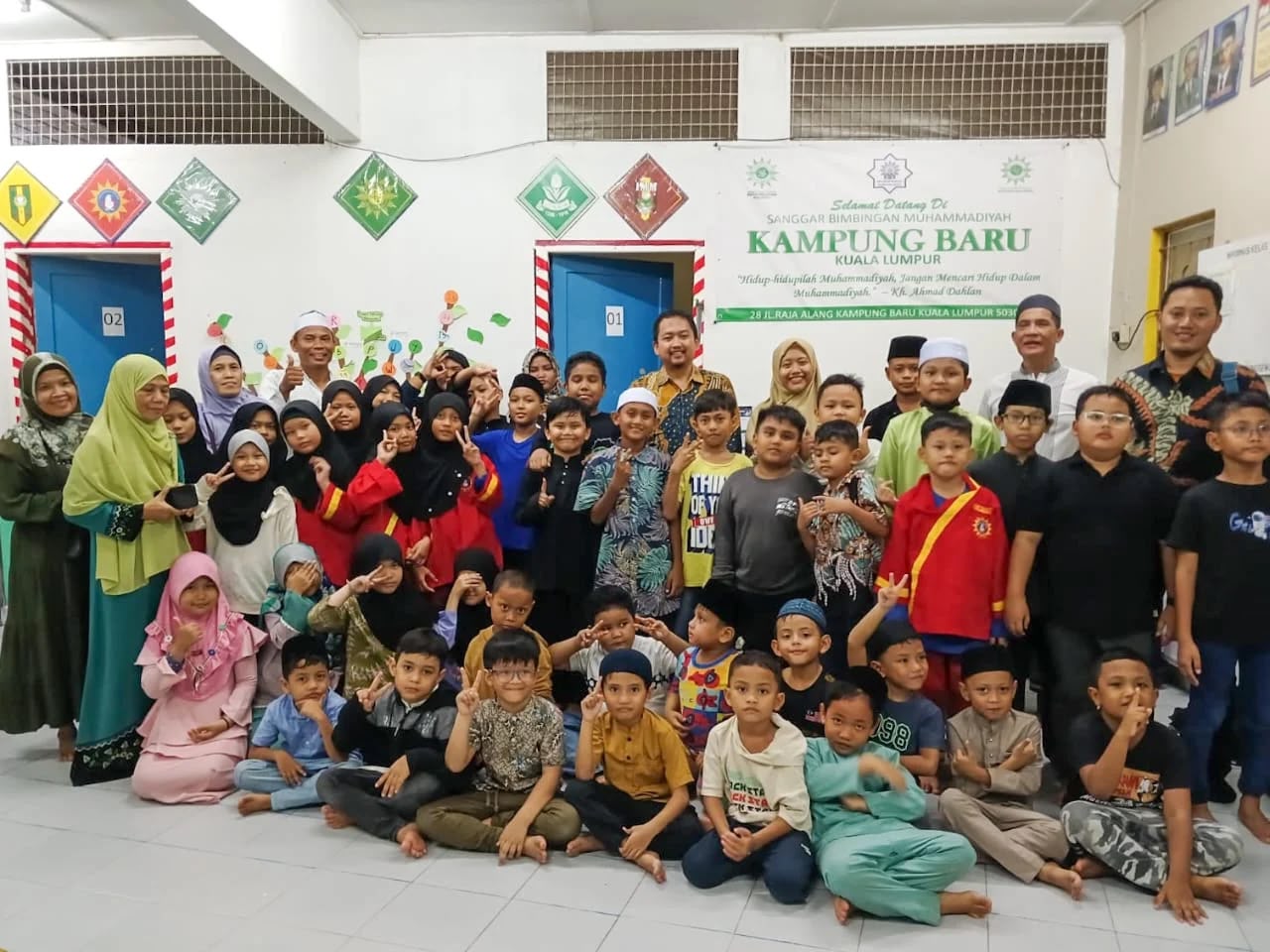 Siswa-siswi dan para pengajar Sanggar Bimbingan Muhammadiyah berfoto bersama dengan pose ceria di dalam ruangan kelas berpapan nama "Sanggar Bimbingan Muhammadiyah Kampung Baru Kuala Lumpur".