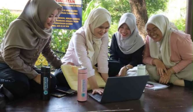 Empat mahasiswi berjilbab sedang belajar bersama menghadap laptop di gazebo taman kampus dengan botol minum/tumbler logo UNIMUS berdiri di atas meja.