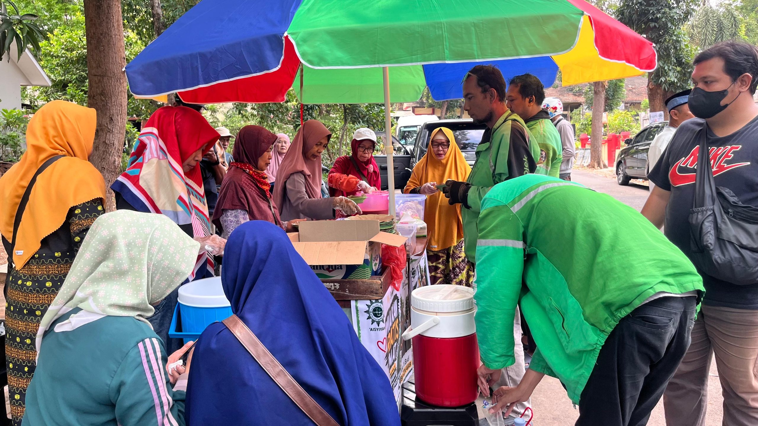 Ibu-ibu pengurus 'Aisyiyah di bawah payung pelangi melayani pembagian porsi makan gratis dan minuman hangat kepada para pengemudi ojek online serta warga di pinggir jalan.