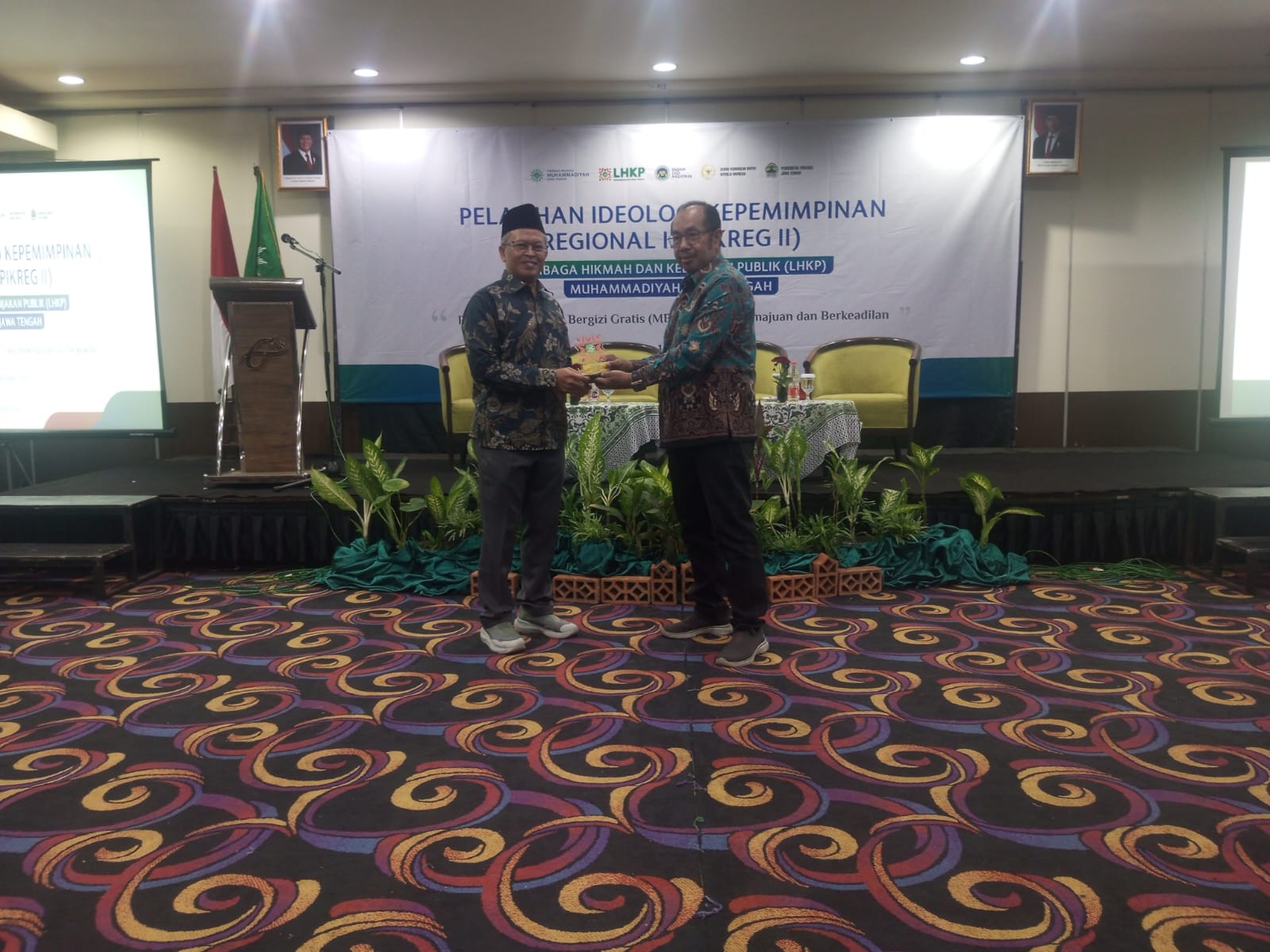 Dua tokoh pimpinan berkemeja batik berdiri bersama di atas panggung penyerahan plakat/cenderamata dengan latar belakang spanduk Pelatihan Ideologi dan Kepemimpinan Regional II (PIGREK II) LHKP Muhammadiyah Jawa Tengah